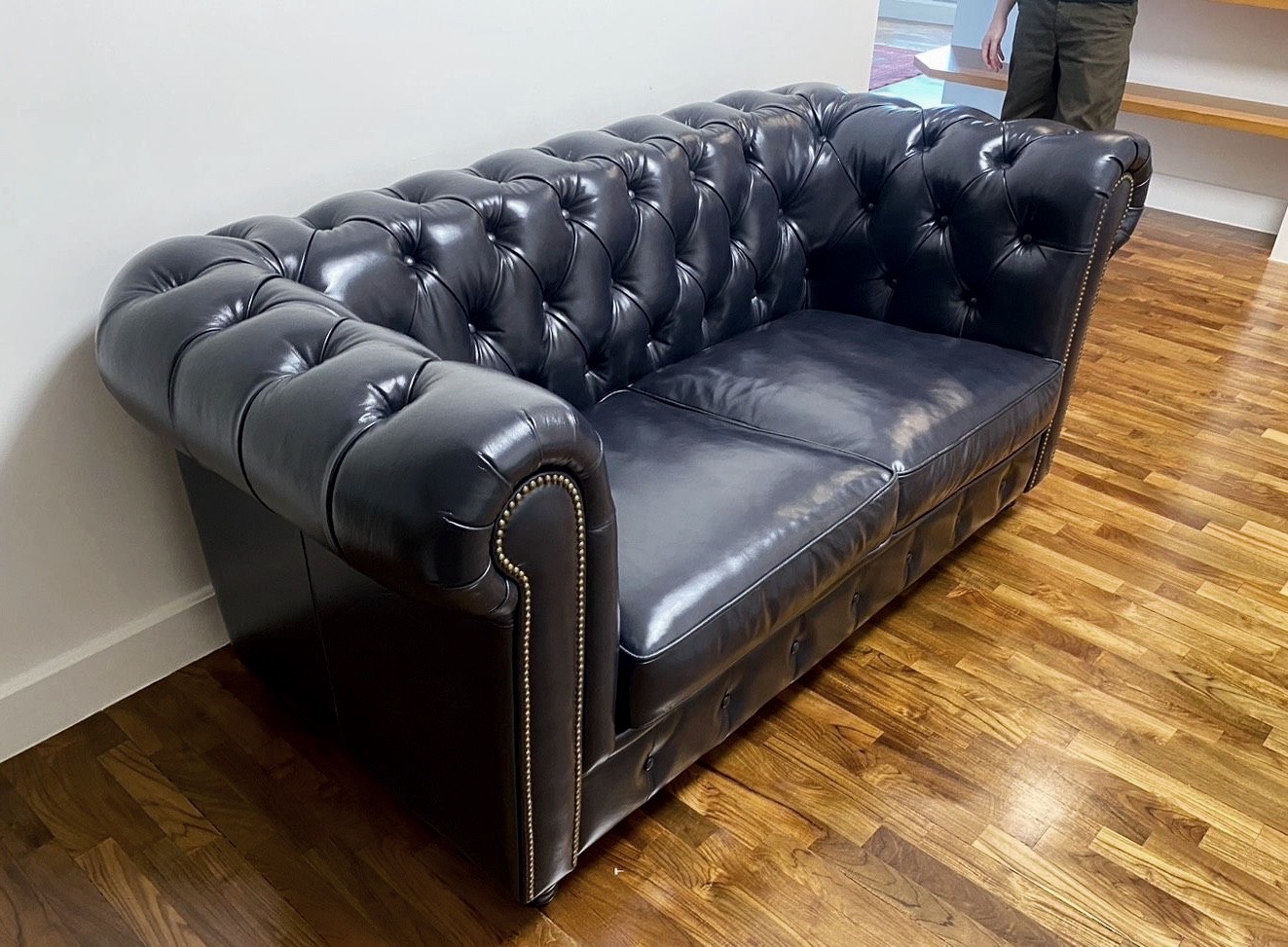 Chesterfield Style B 頂級油蠟黃牛皮沙發側視圖，完美呈現深炭藍皮革原生紋理、純手工深層菱格拉扣工藝，以及邊緣精準俐落的黃銅鉚釘收邊細節。